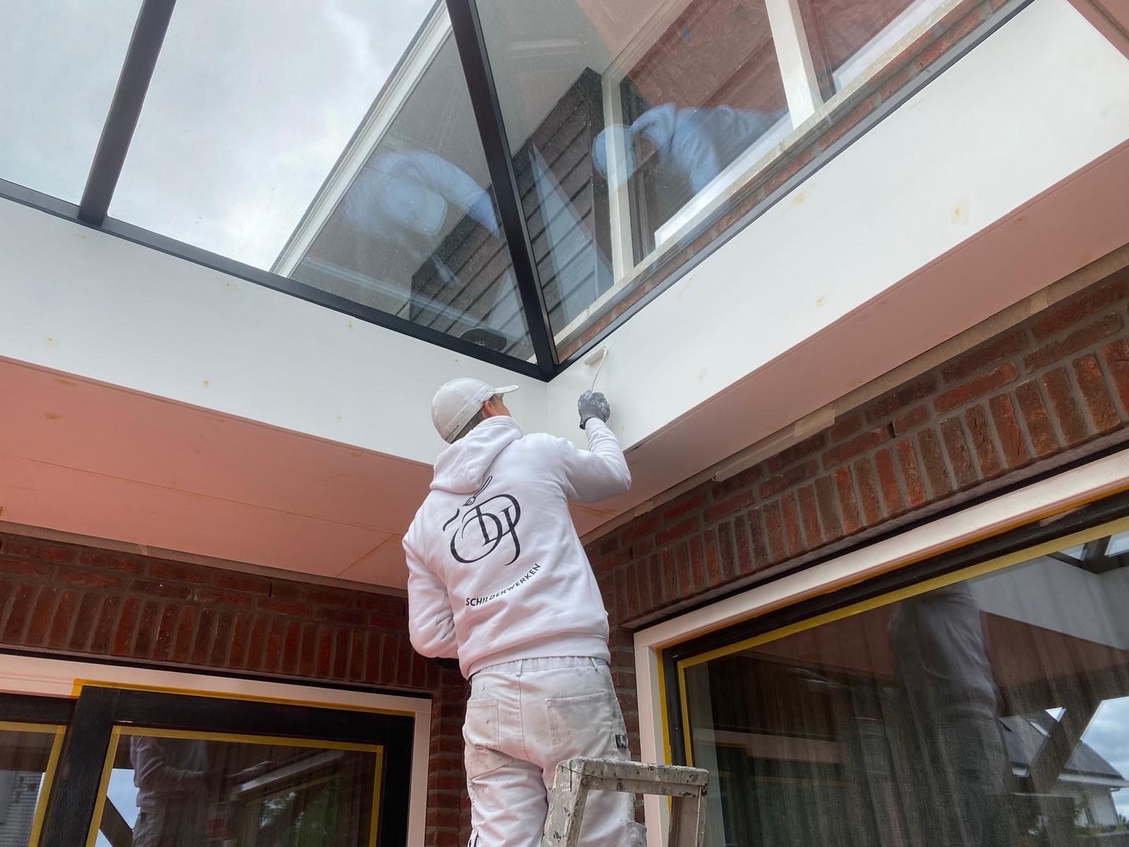Een man staat op een ladder en schildert een raam.