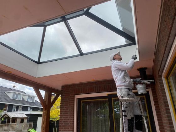 Een man staat op een ladder en schildert het plafond van een huis.