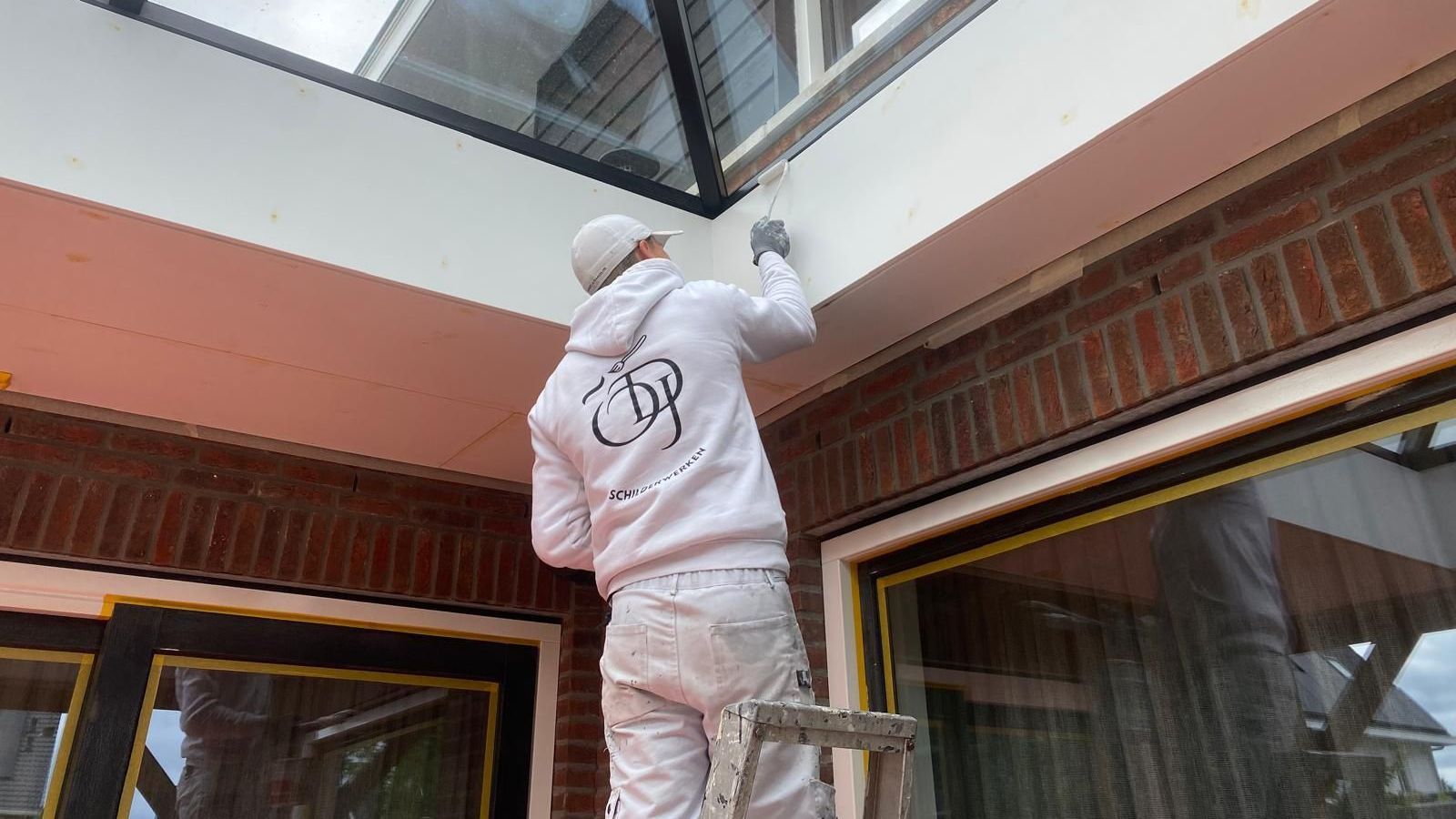 Een man staat op een ladder en schildert een gebouw.