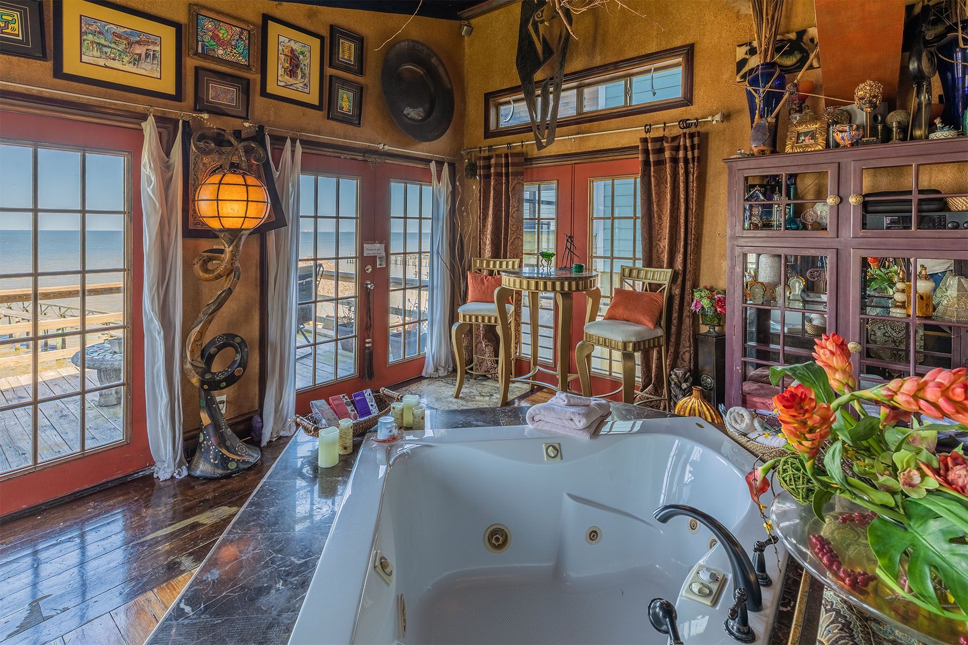 Bathroom with a jacuzzi tub overlooking a beach. Ornate decor, red doors, and warm tones.