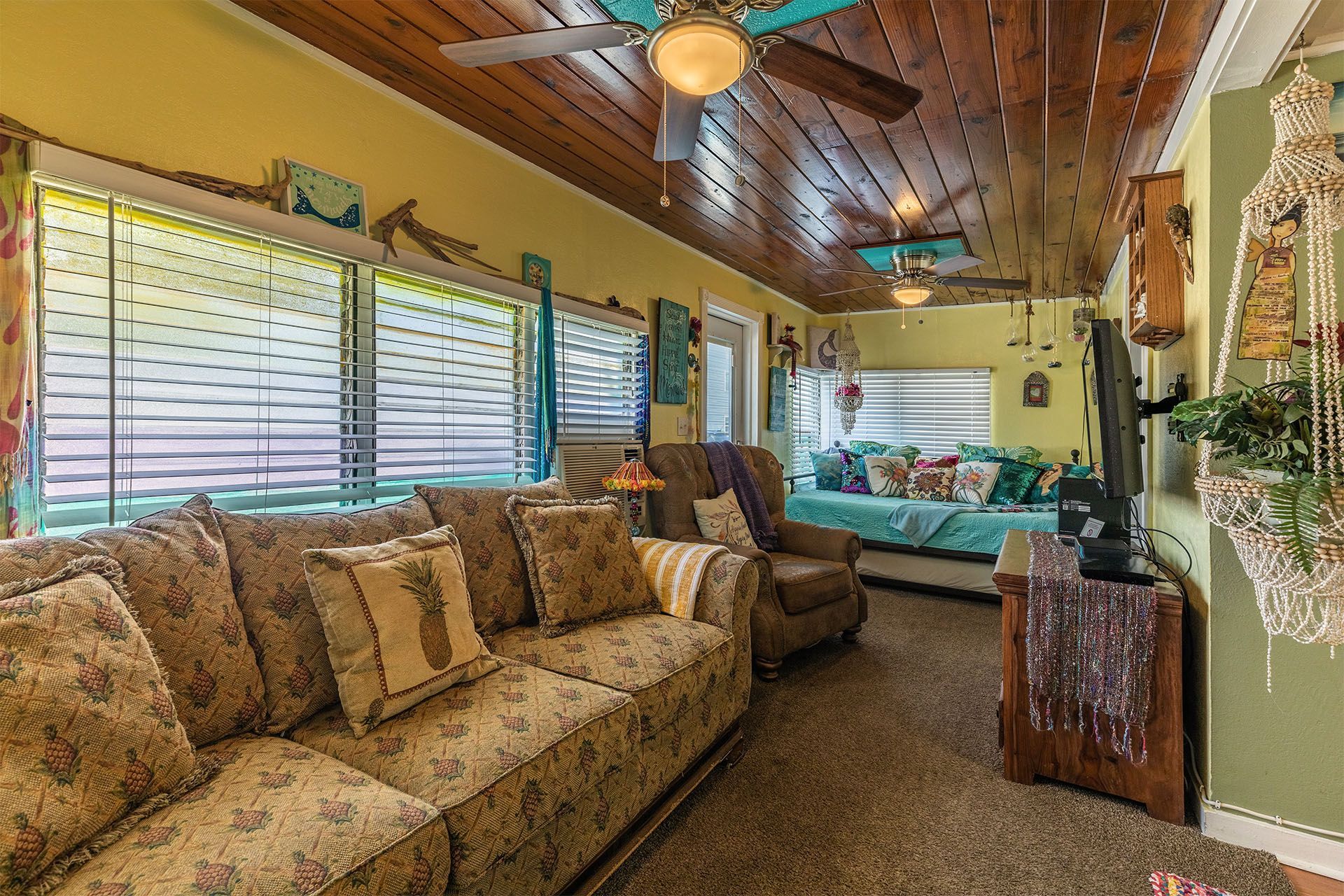 Cozy living room with floral couch, wood ceiling, green walls, and large windows.