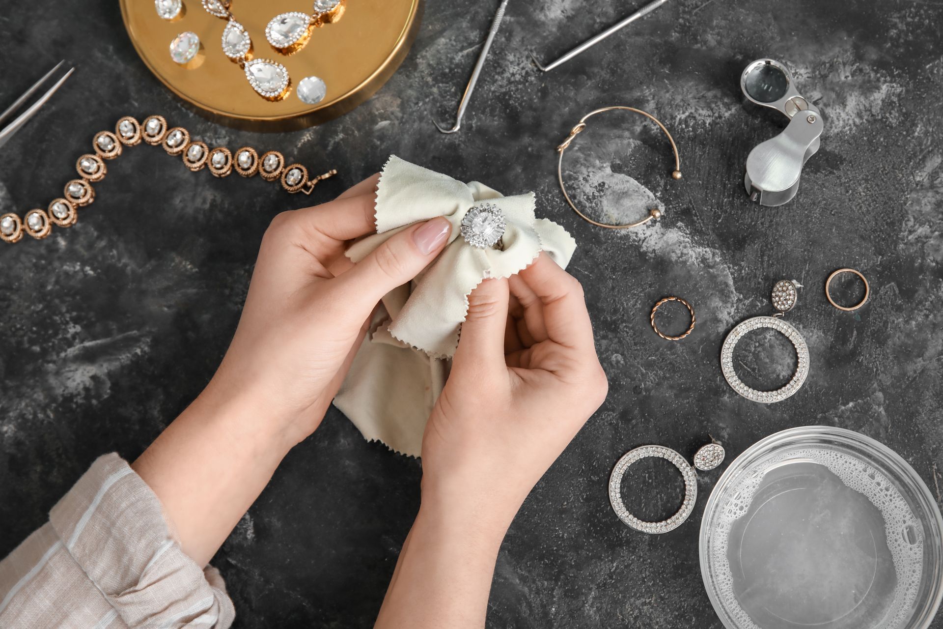 A woman is cleaning jewelry with a cloth on a table.