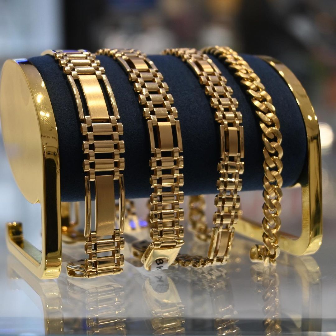 Four gold bracelets displayed on a blue velvet cushion, on a gold stand.