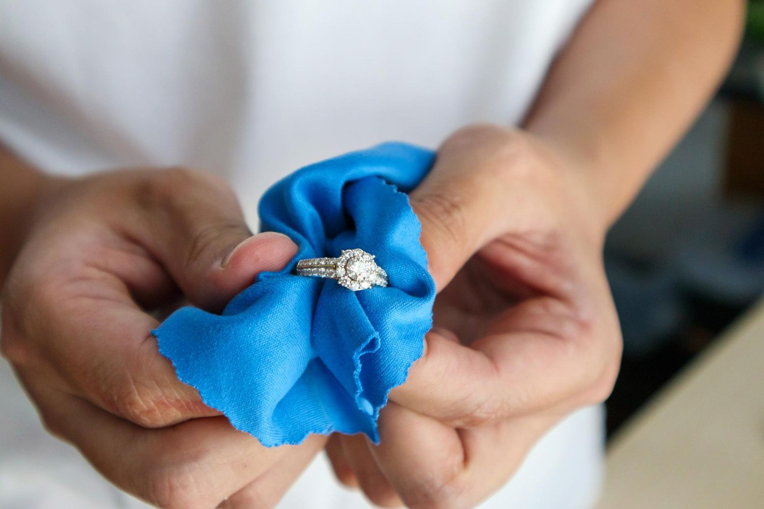 Person holding a diamond ring in a blue cloth for cleaning.