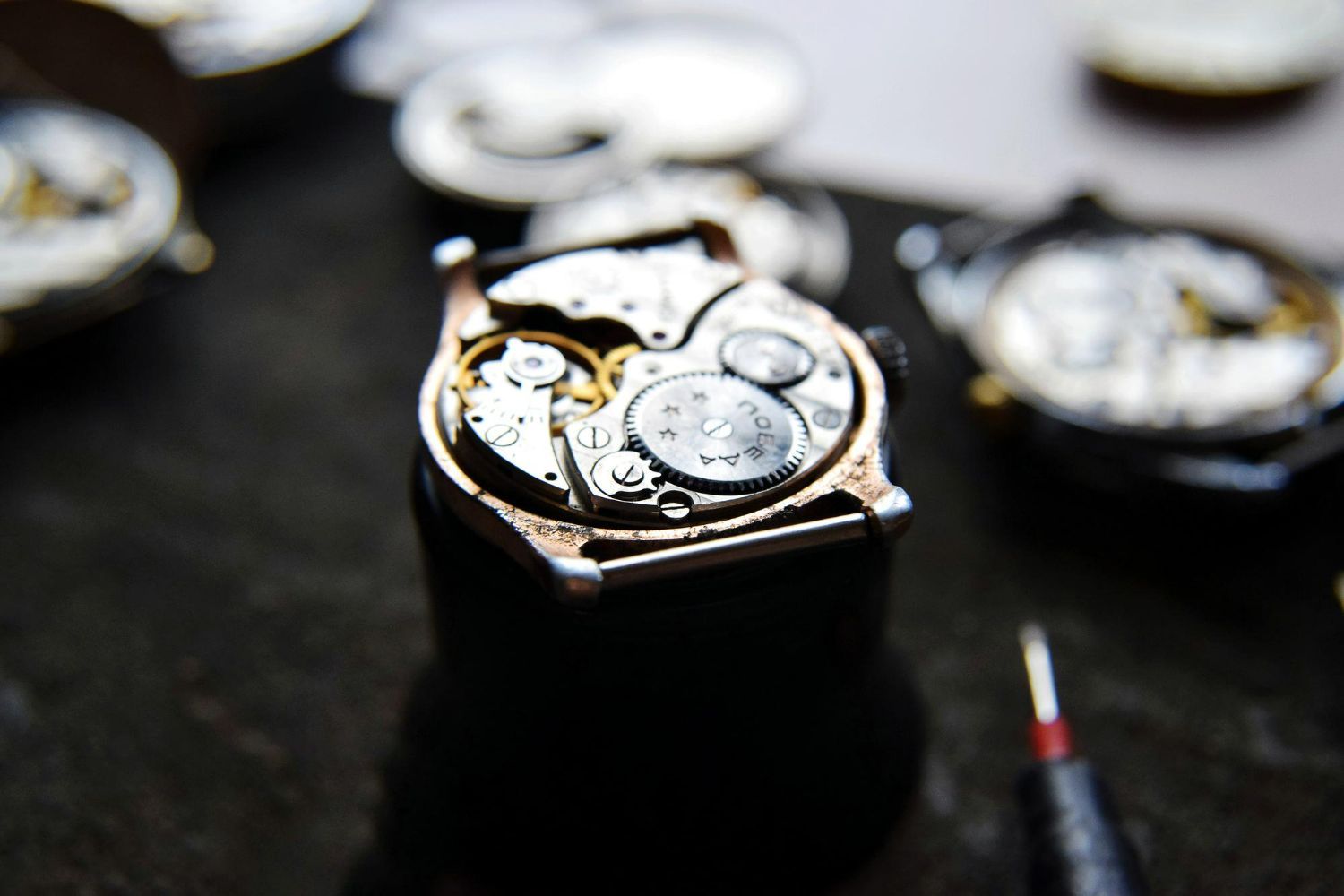 Watch mechanism, disassembled, in a workshop setting, with tools.