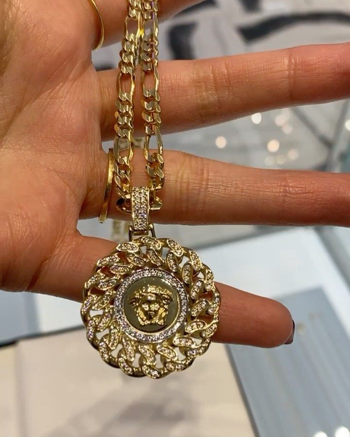 A person is holding a gold necklace with a medusa pendant