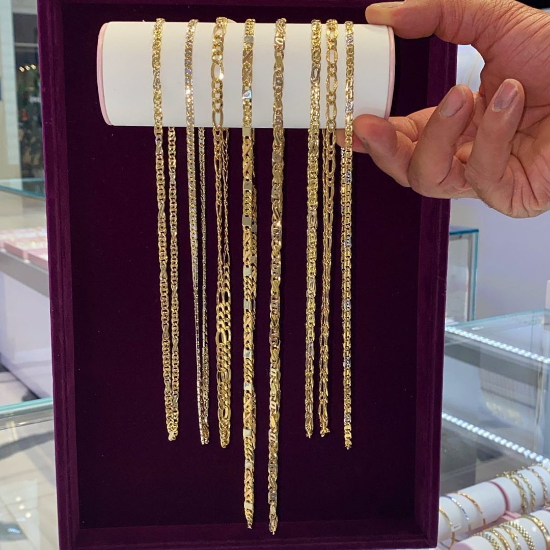A person is holding a display of gold chains in a purple box