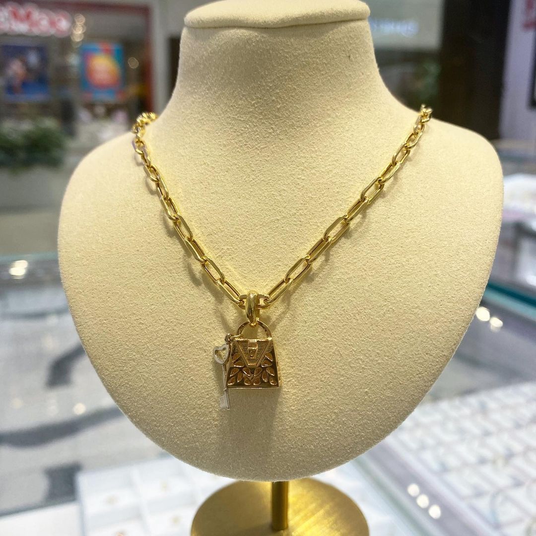 A gold necklace with a padlock pendant is on a mannequin.