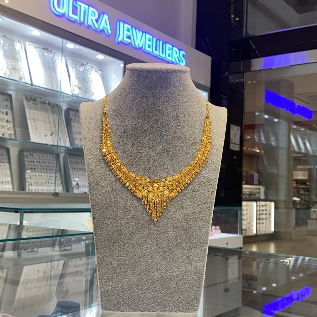 A gold necklace on a mannequin in front of a sign that says ultra jeweller 's