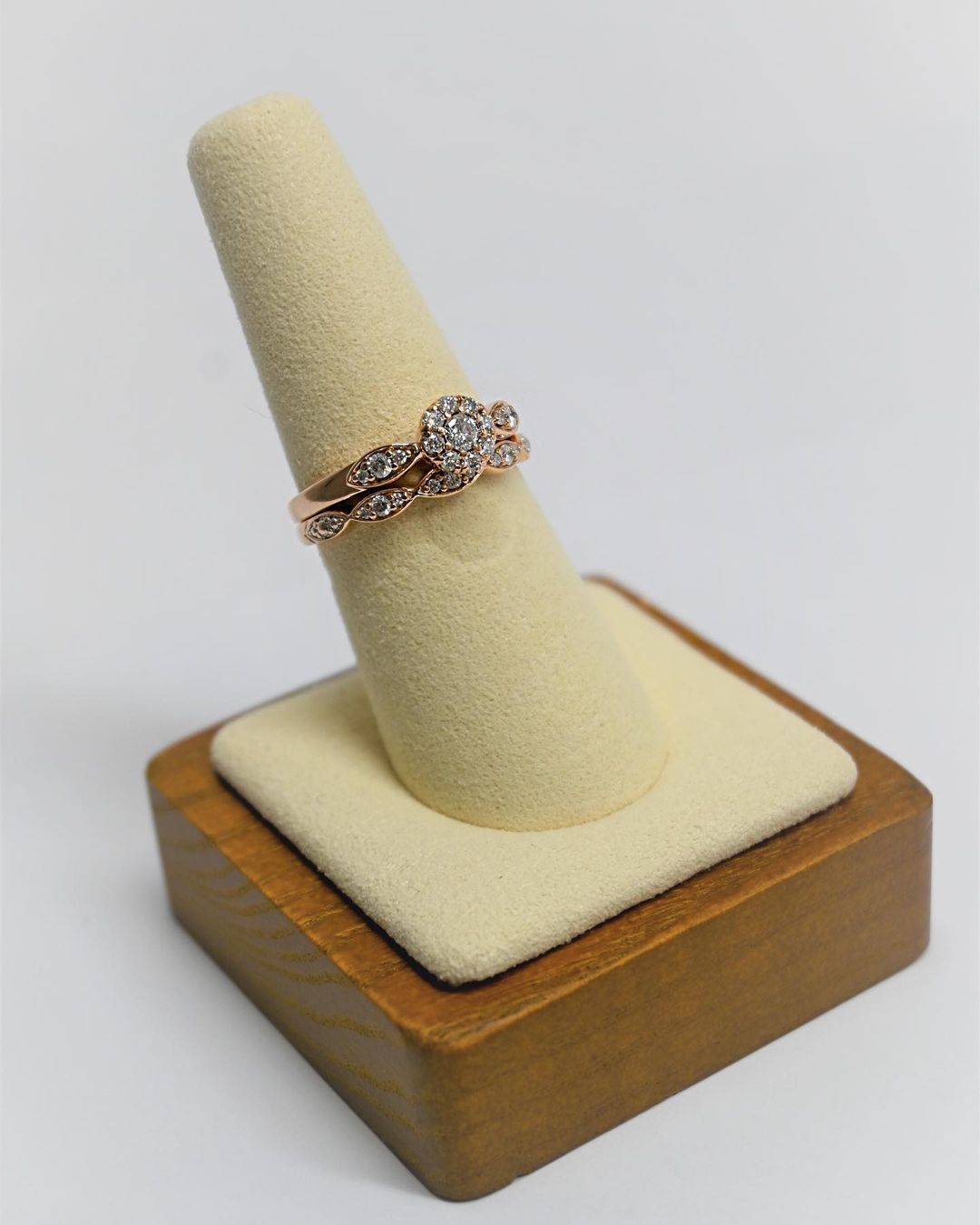 Rose gold diamond ring set on a beige ring display, set on a wooden block against a white background.