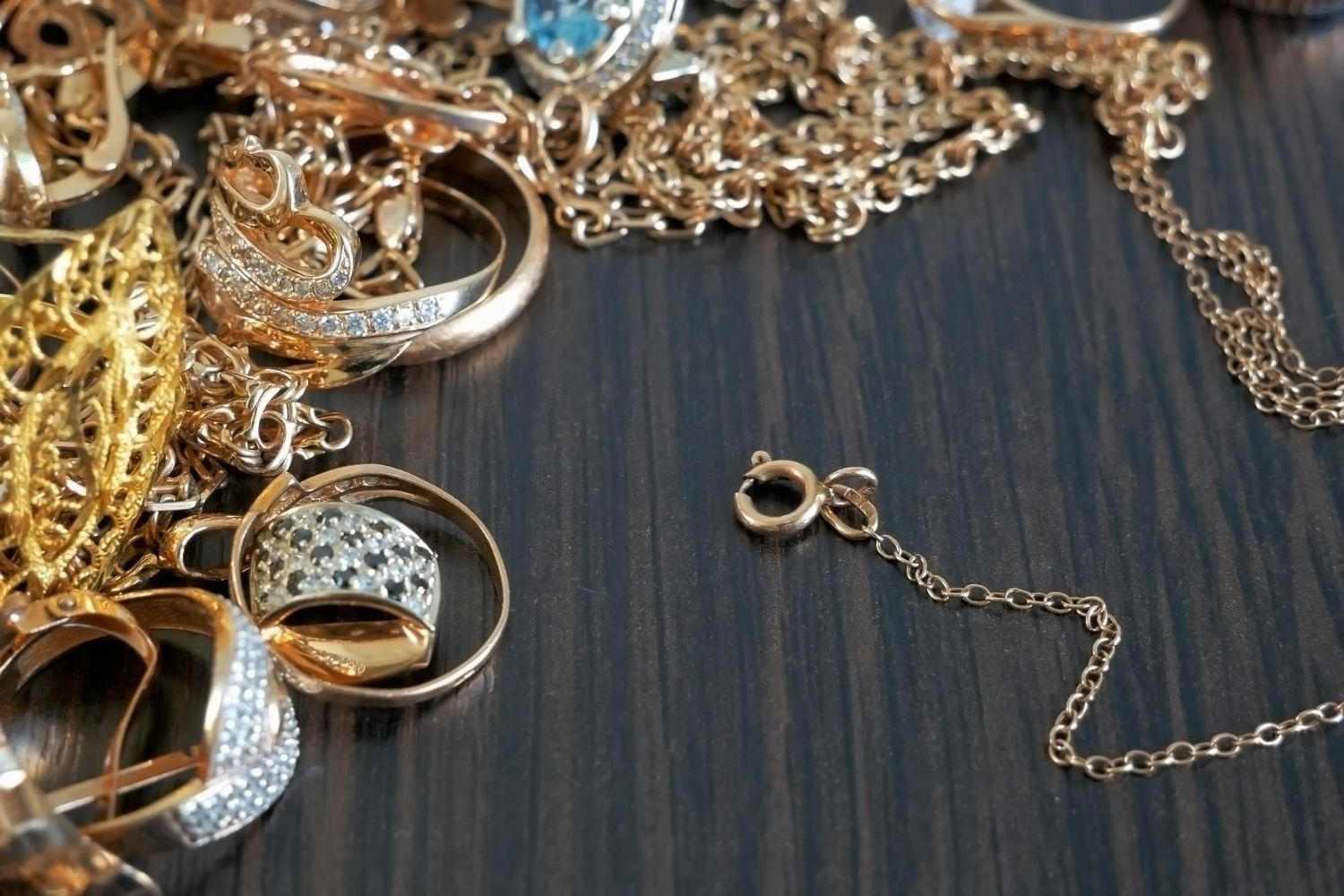 A collection of gold jewelry, including rings, chains, and earrings, rests on a dark wooden surface.