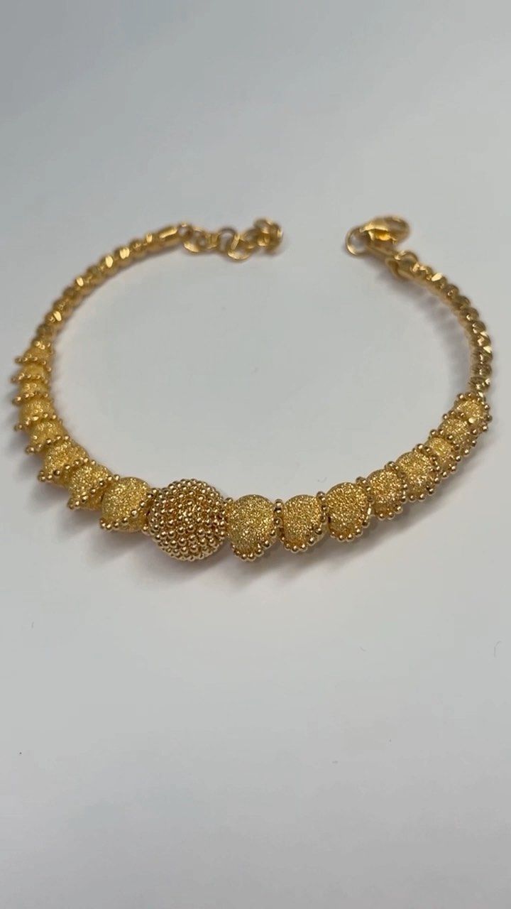 A close up of a gold bracelet on a white surface.