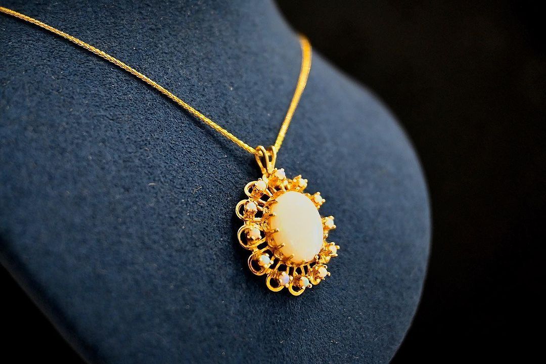 A gold necklace with a white pendant on a mannequin