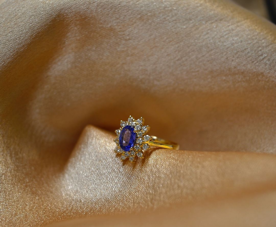 A gold ring with a blue stone and diamonds on a cloth.