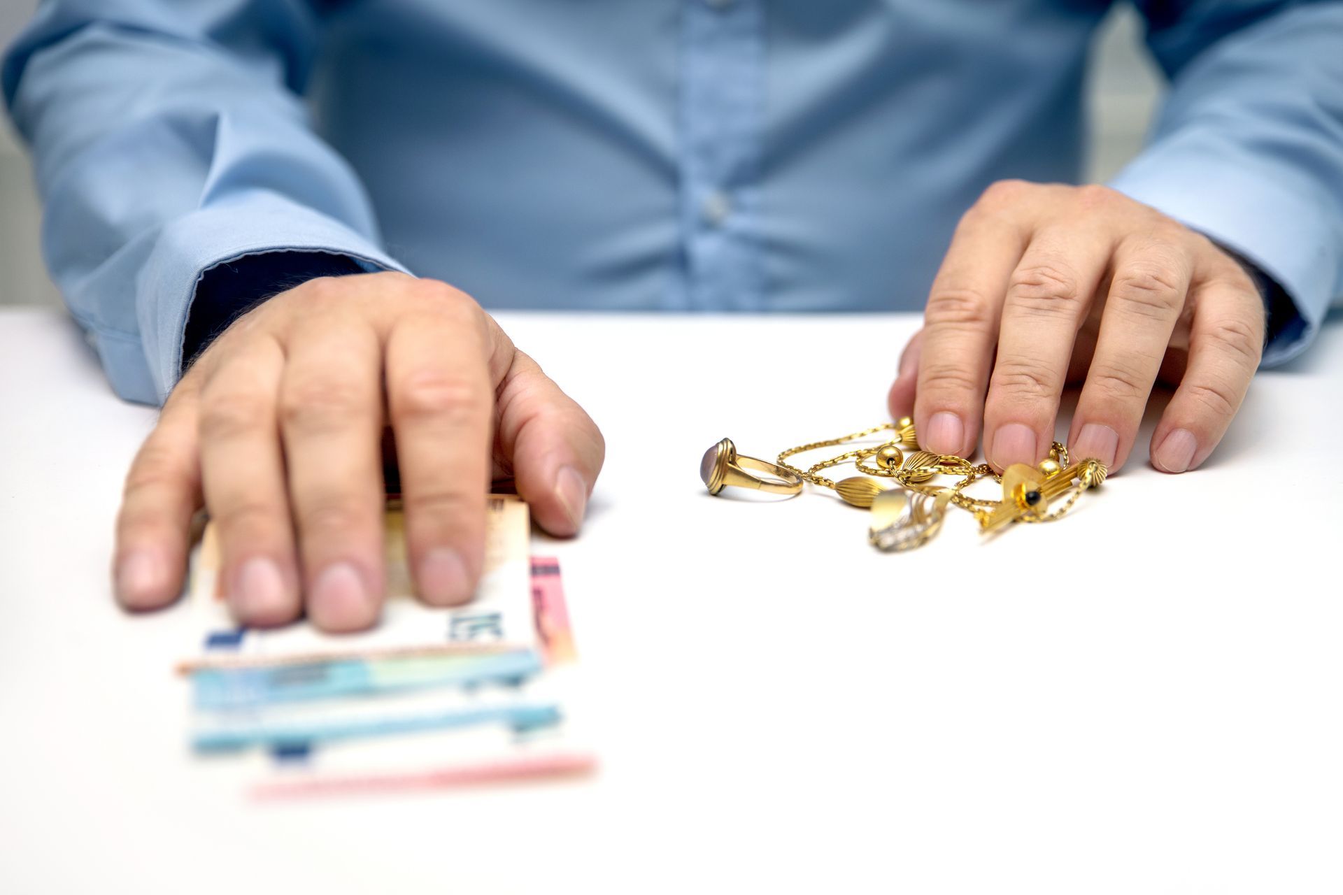 A man is sitting at a table holding a bunch of money and gold jewelry.