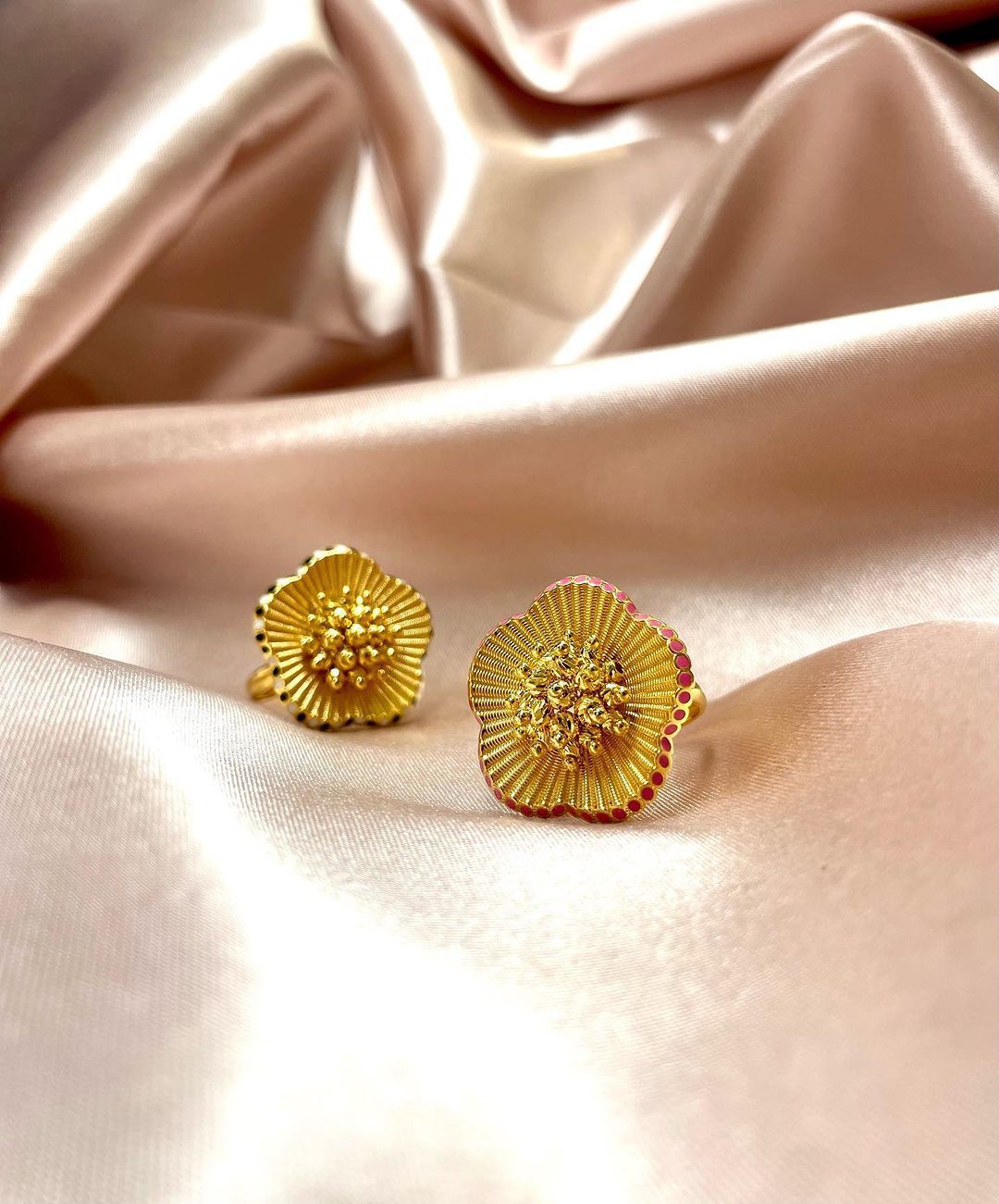 Gold flower-shaped stud earrings resting on a soft, peach-colored satin fabric.