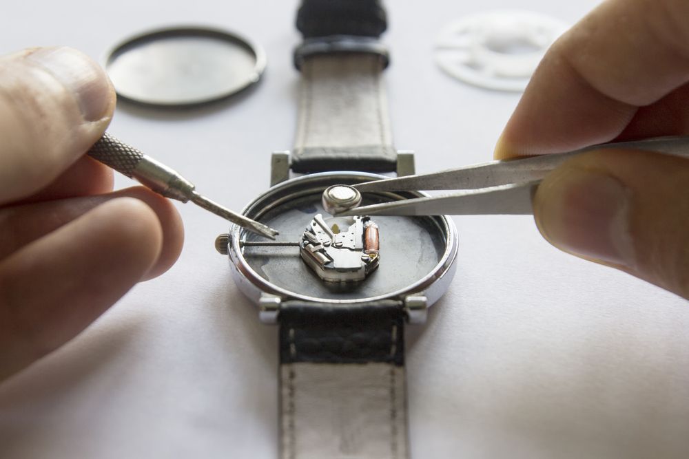 A person is fixing a watch with tweezers and a screwdriver.