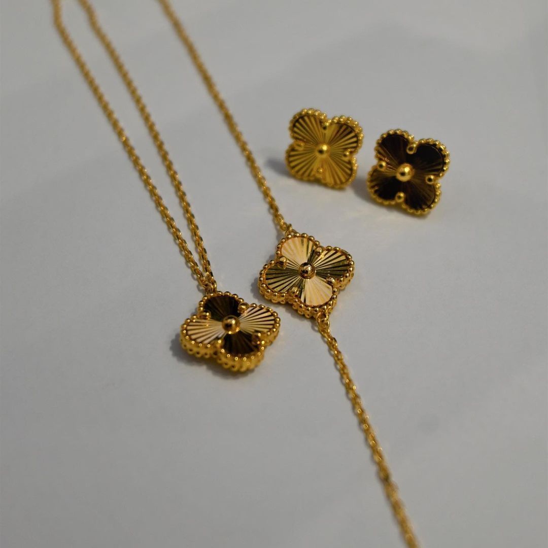 Gold clover-shaped jewelry set: necklace, bracelet, and earrings on a white surface.