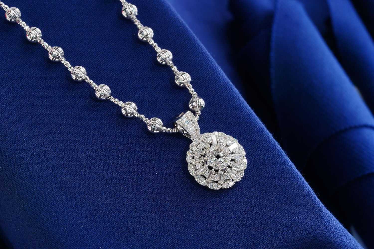 A diamond-encrusted pendant necklace lies on a textured, deep blue fabric.