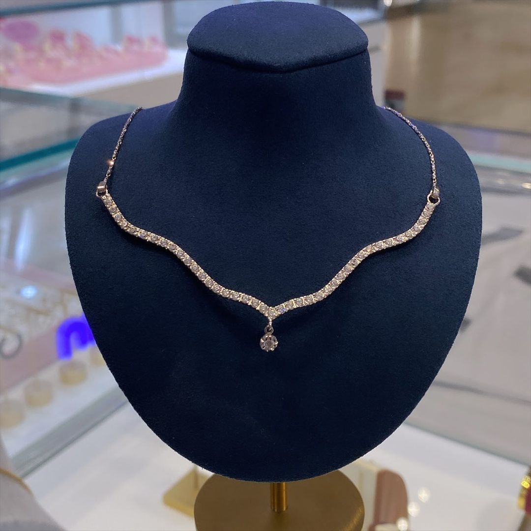 Diamond necklace on a blue display bust with a wave-like design and a dangling pendant.