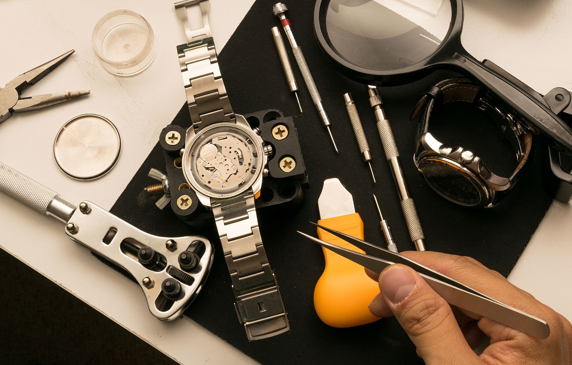 A person is working on a watch with a pair of tweezers.
