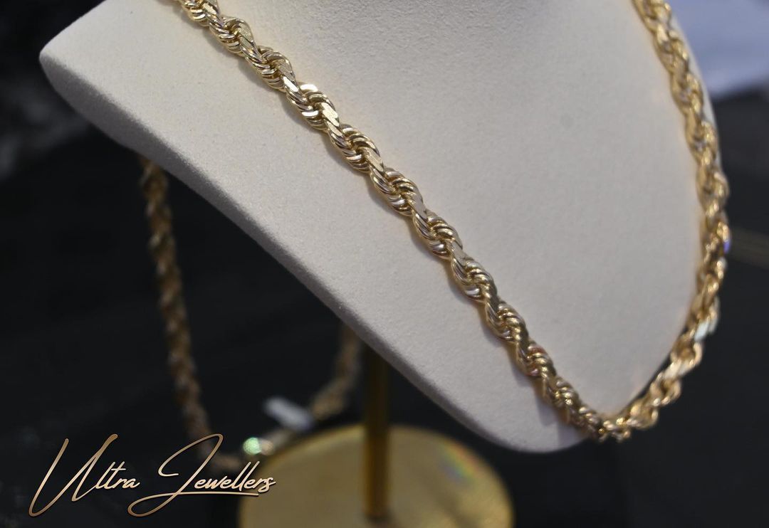 Gold rope chain necklace displayed on a white jewelry bust, in a store setting.