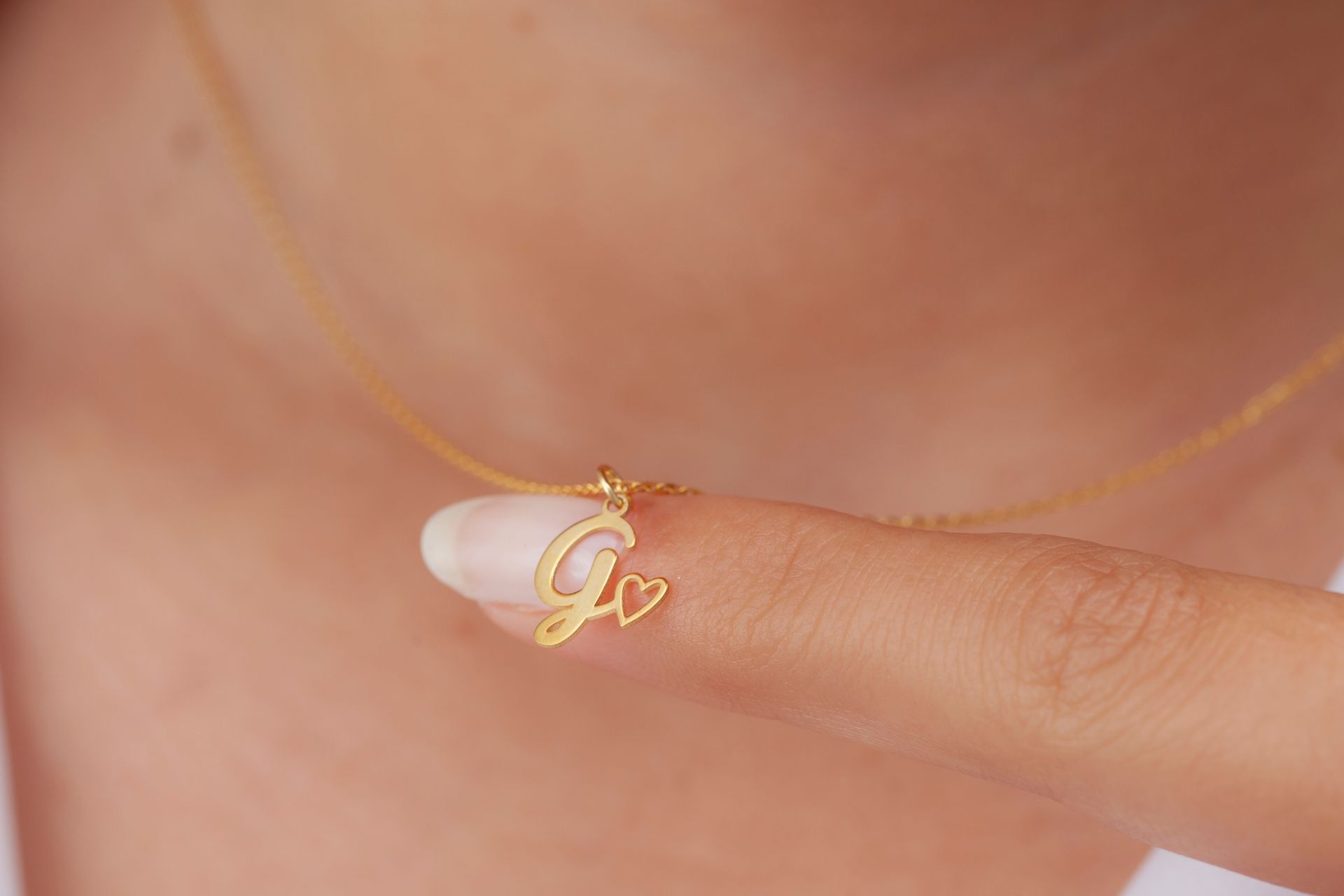 A woman is wearing a gold necklace with a letter g and a heart.