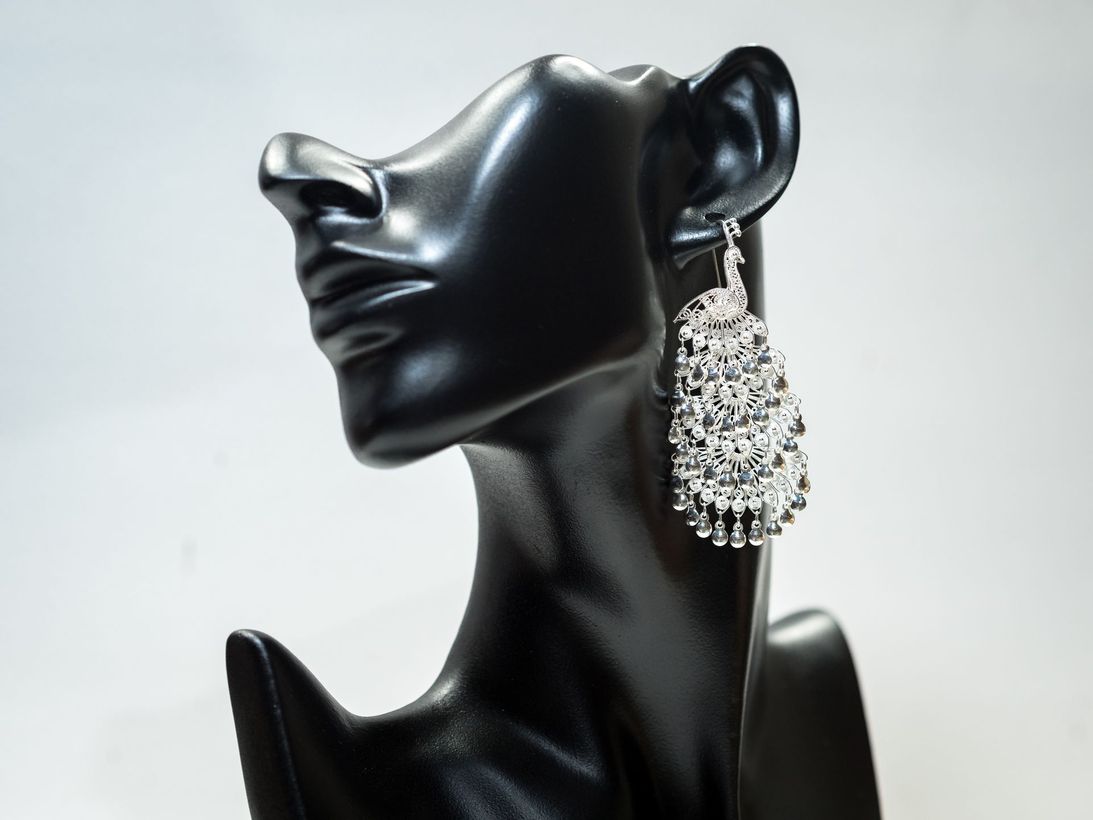 A black mannequin wearing a pair of silver earrings