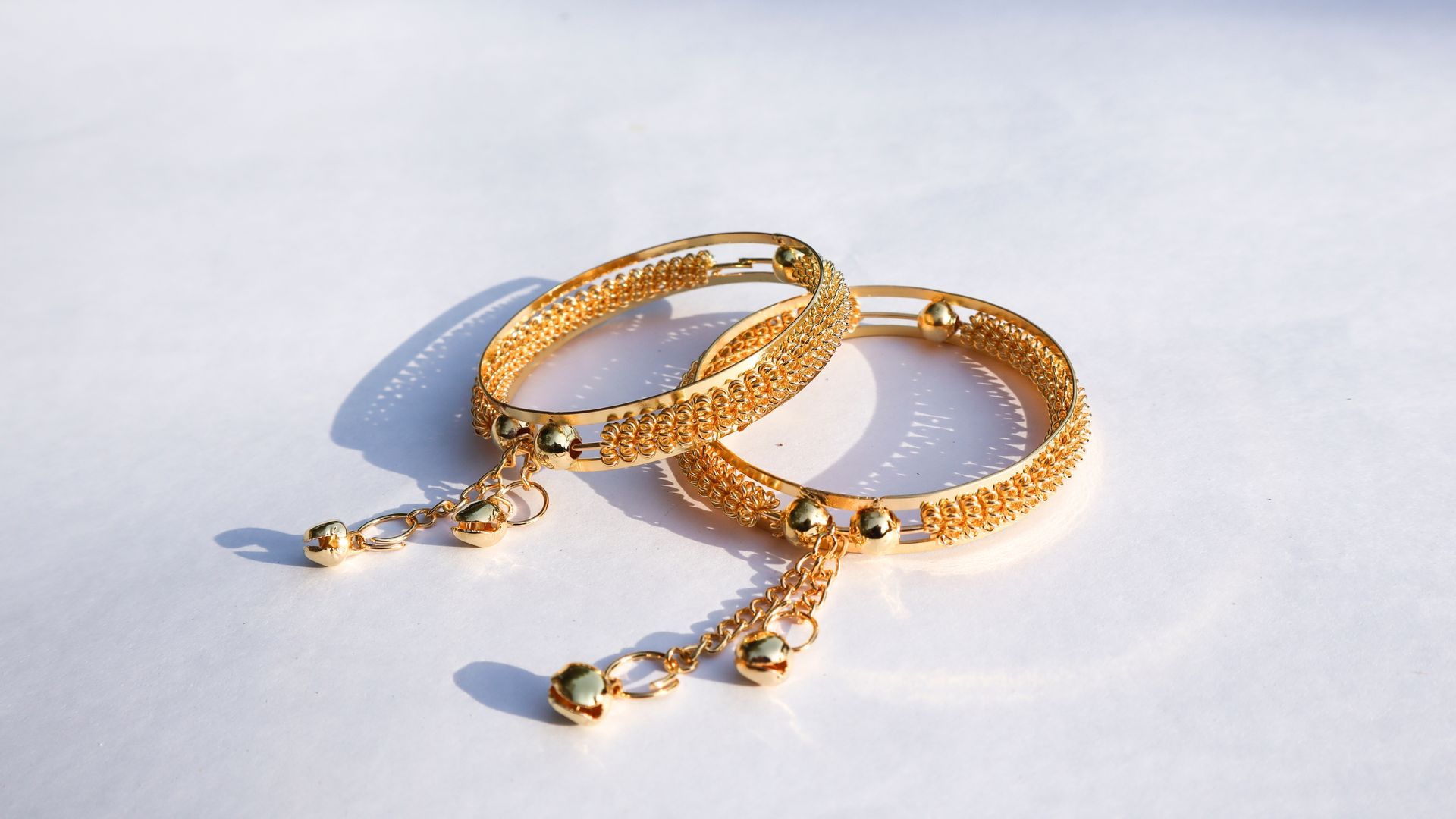 A pair of gold bracelets on a white surface.