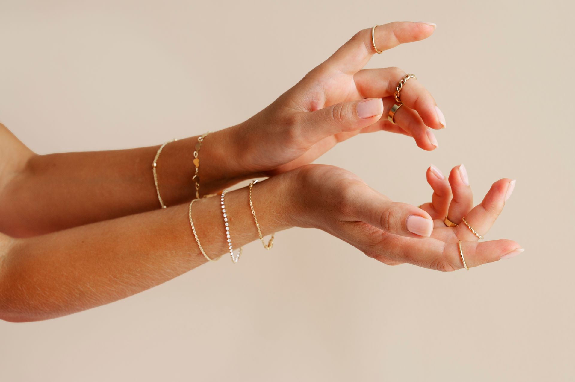 Hands adorned with gold jewelry against a light background.