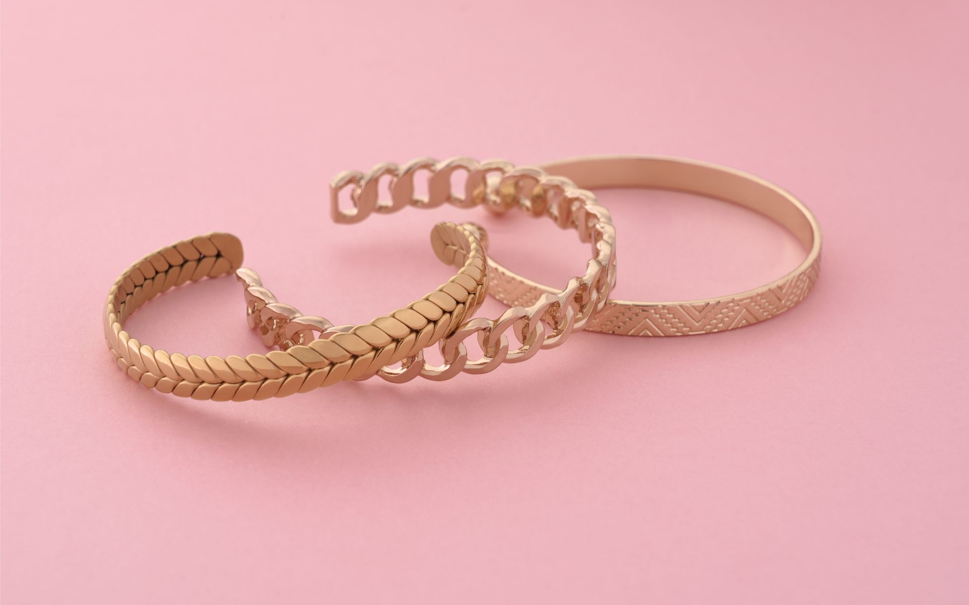 Three gold-colored bracelets on a light pink background.