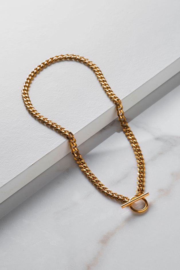 A gold necklace is sitting on a white surface.