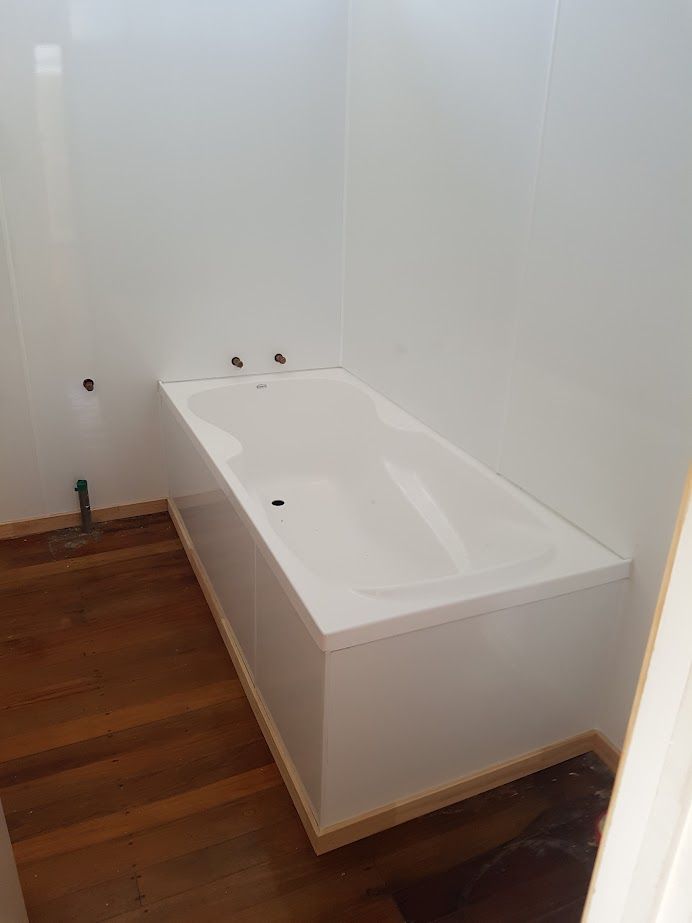 Featured is a pristine bath installation, cradled within the sleek durability of Aluminum Composite Panels for both the cradle and walls, complemented by classic timber skirting and hardwood flooring. The bath awaits final fittings by the plumber to complete this harmonious blend of modernity and tradition.