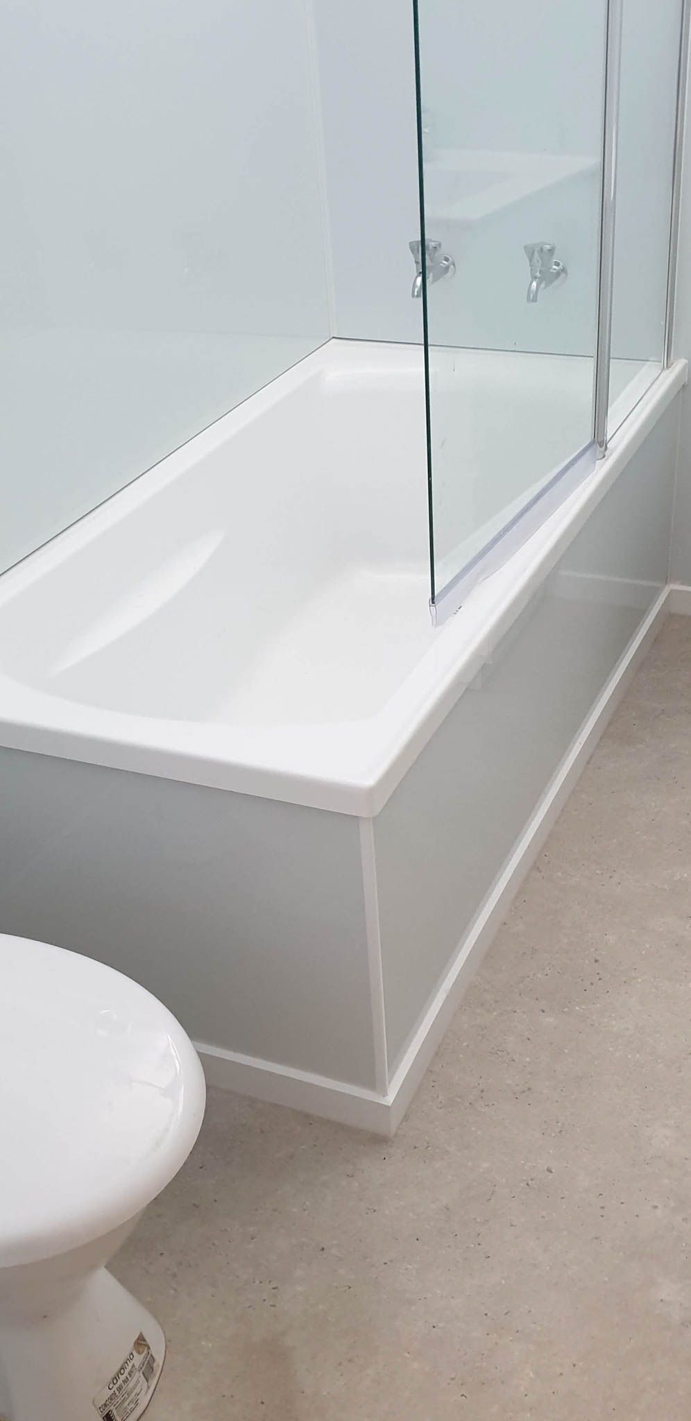 Showcasing a fusion of practical design and sleek aesthetics, this bathroom features a bath and shower area secured by a transparent glass door. The surrounding walls are fitted with Aluminum Composite Panel sheets, chosen for their superior waterproof qualities and durability. The floor boasts a hard-wearing vinyl covering, selected for its longevity and ease of cleaning, perfect for a busy bathroom setting.