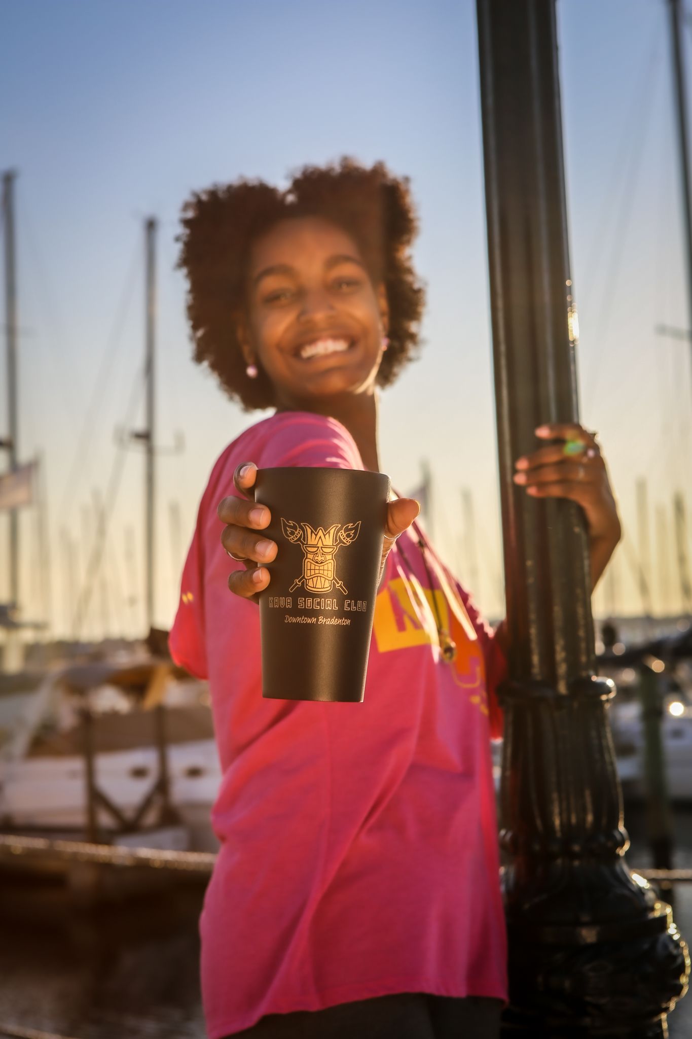 A woman in a pink shirt is holding a black cup and smiling.