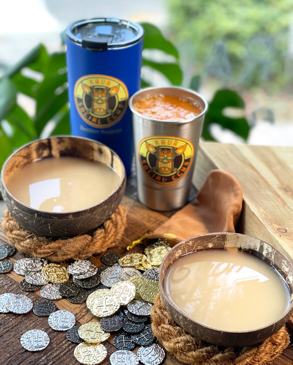 Three cups of liquid are sitting on a wooden table surrounded by coins.