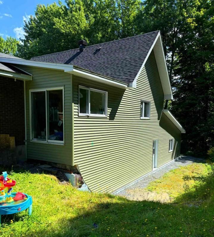 Une maison verte avec un toit noir est entourée d'arbres