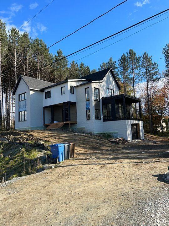 Une grande maison blanche est située au sommet d'une colline de terre entourée d'arbres.
