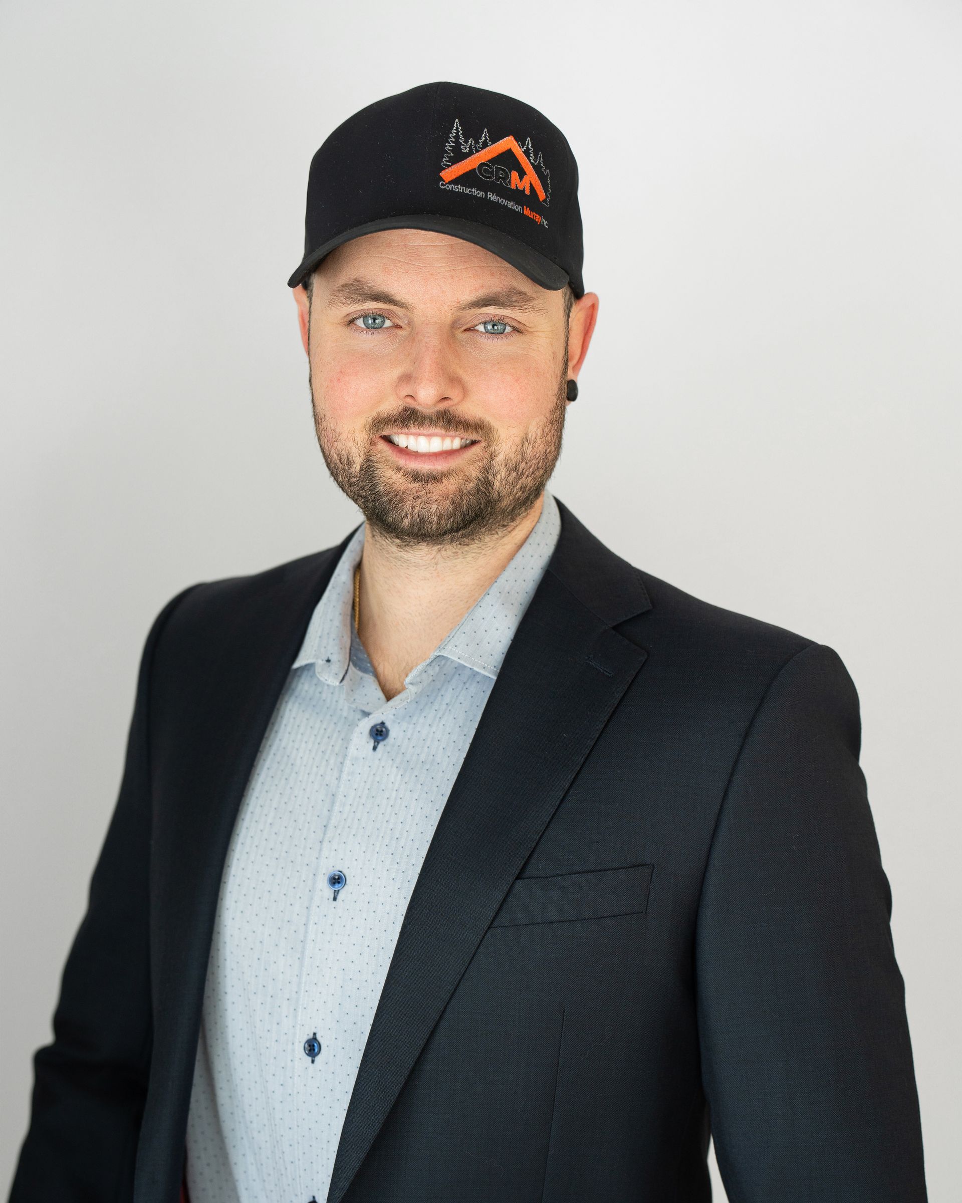 Un homme en costume et chapeau sourit à la caméra.