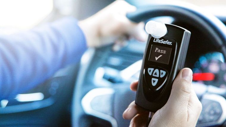Person holding a black breathalyzer while seated in a car