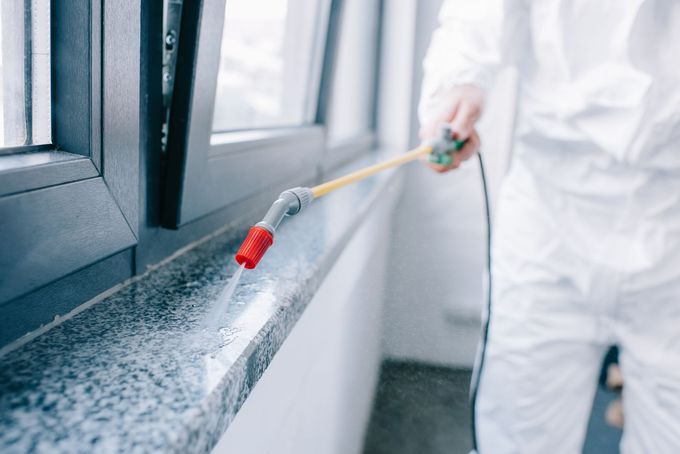 Una persona con indosso una tuta protettiva bianca utilizza uno spruzzatore manuale per applicare un trattamento chimico a un davanzale in pietra.