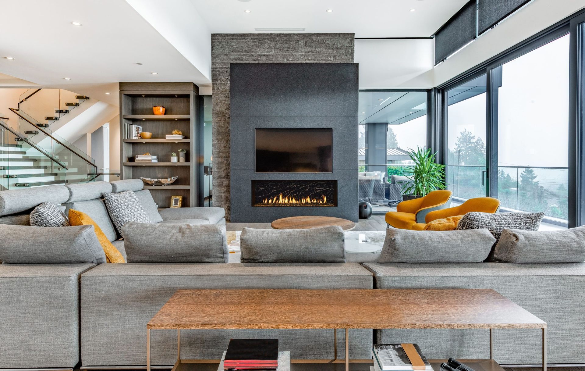 Modern living room with a gray sectional sofa, fireplace, and large windows with a view.