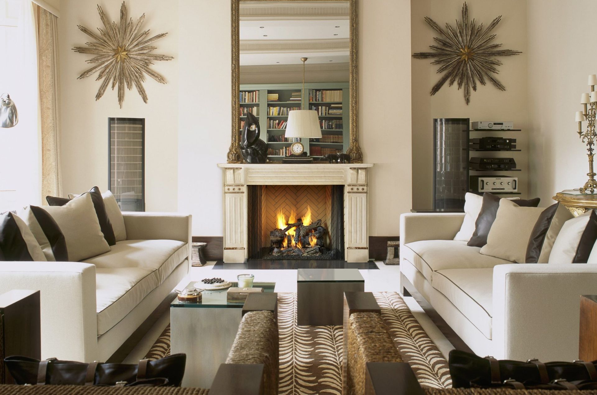 Living room with fireplace, sofas, large mirror, and starburst wall decor. Warm colors and classic design. Living room with fireplace, sofas, large mirror, and starburst wall decor. Warm colors and classic design.