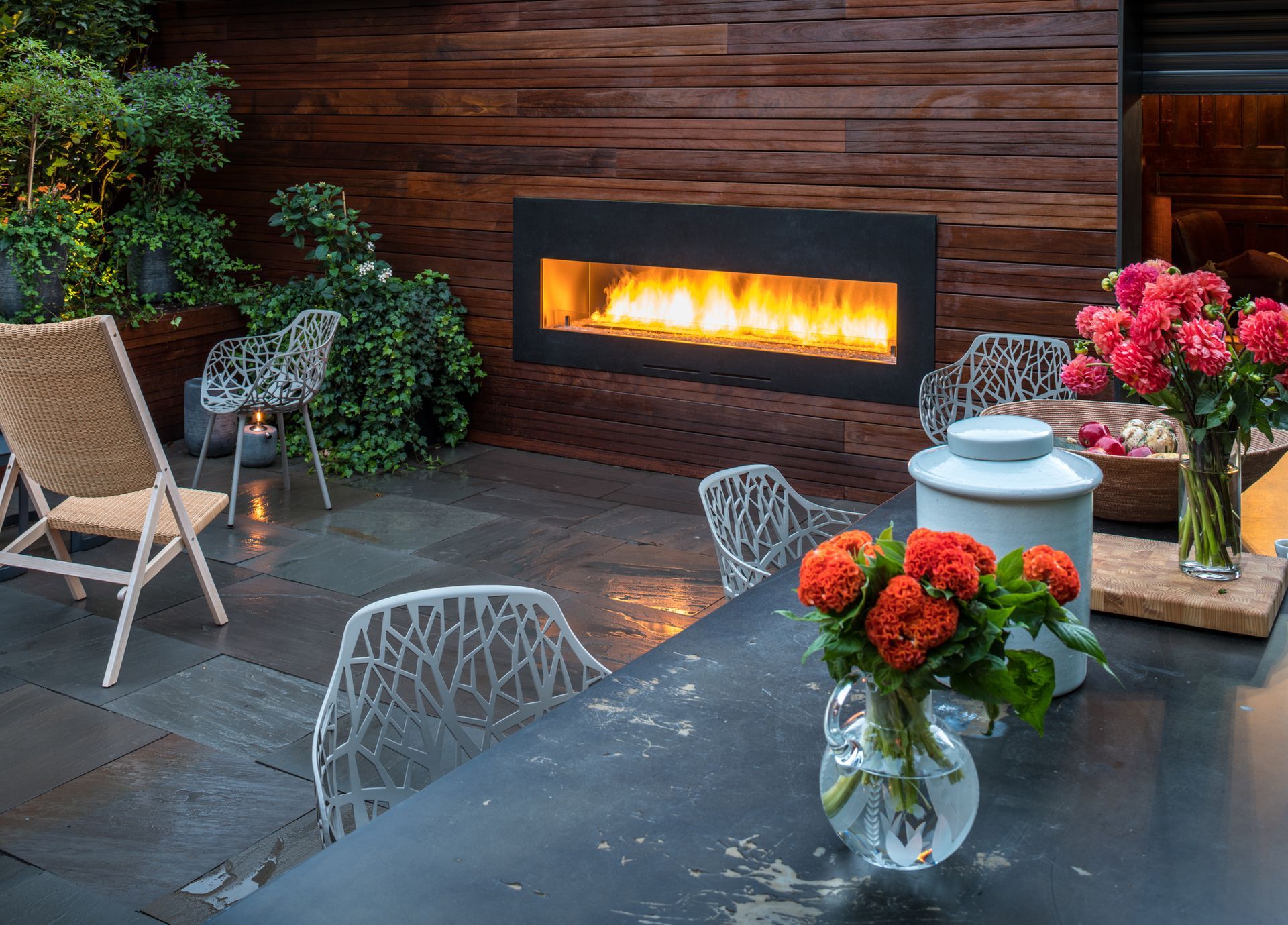 Outdoor patio with fireplace, seating, flowers, and wooden wall.