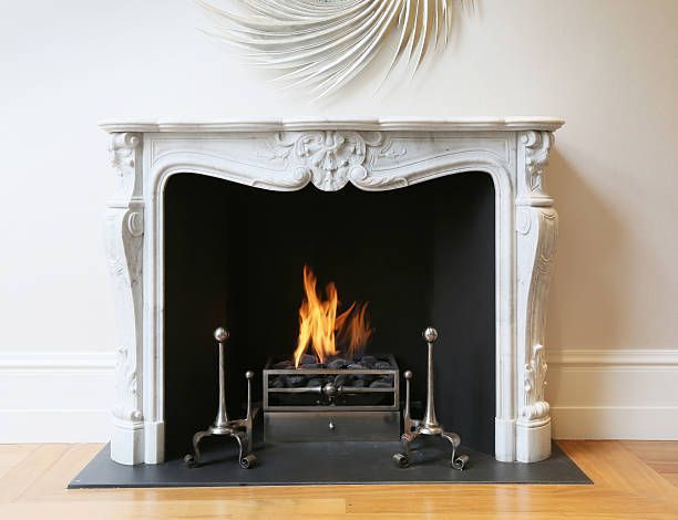 Ornate white fireplace with fire burning inside. Silver tools stand in front.
