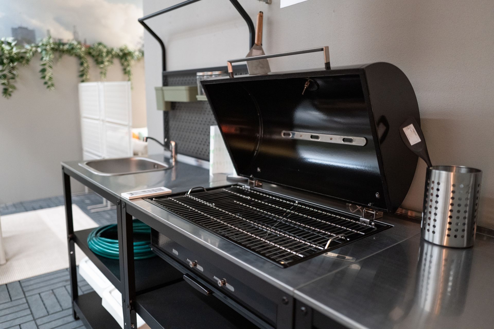 Black grill with open lid on a stainless steel outdoor kitchen counter.