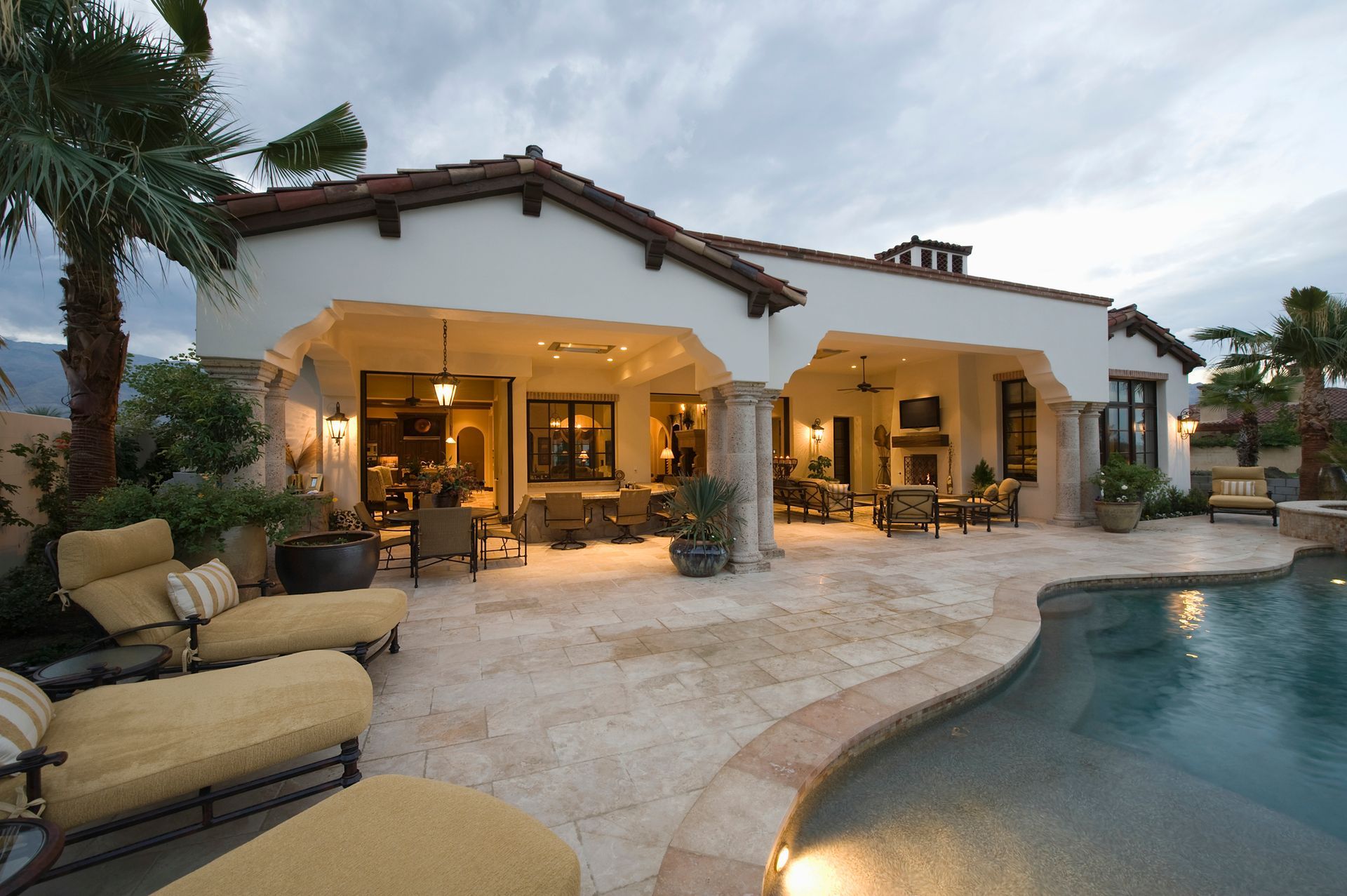 Exterior view of a luxury home with a pool and patio. The sky is overcast.