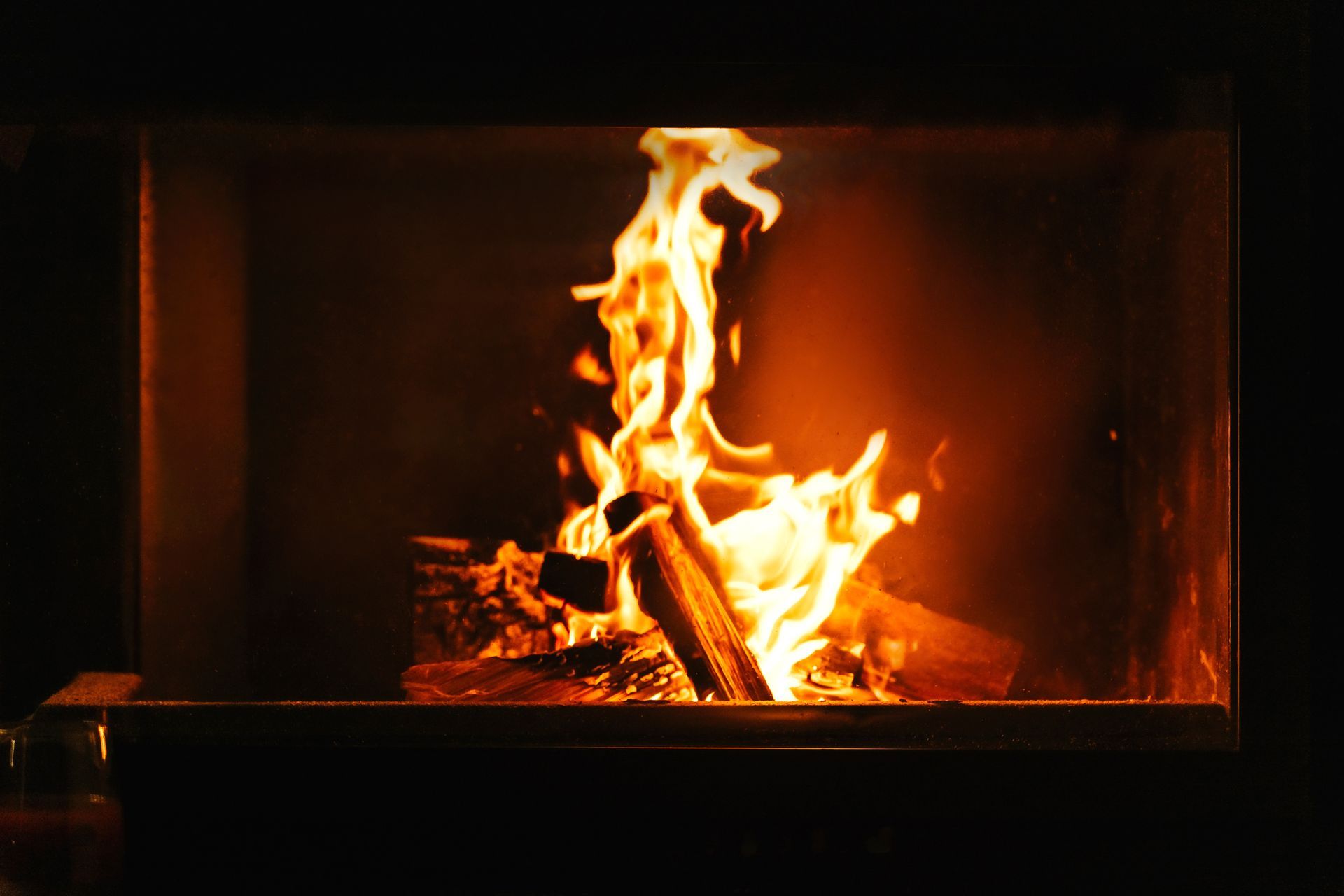 Fire burning brightly in a fireplace, with orange and yellow flames against a dark background.