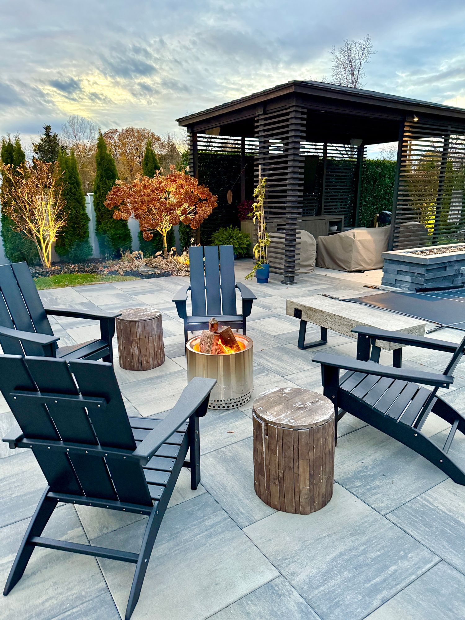 Outdoor seating area with a fire pit, Adirondack chairs, and a gazebo on a stone patio.