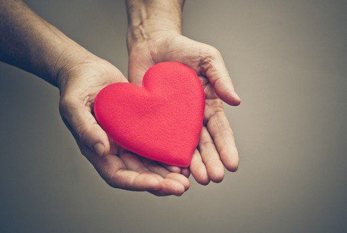 A person is holding a red heart in their hands.